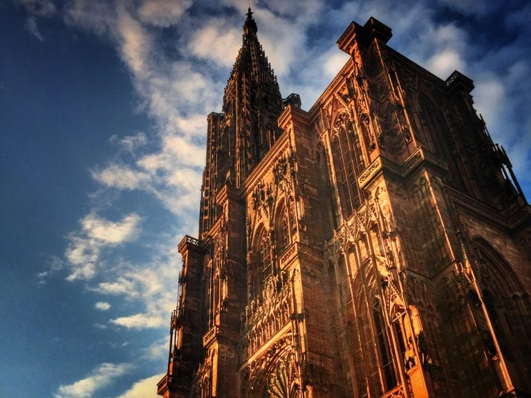 Céu azul com nuvens brancas com a Catedral Gótica de Notre Dame de Strasbourg vista em contra-plongee (de baixo para cima)