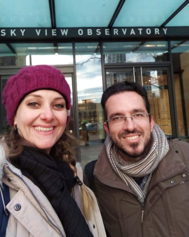 Selfie da Chai e do Augusto em frente a porta do prédio onde se lê "Sky View Observatory"