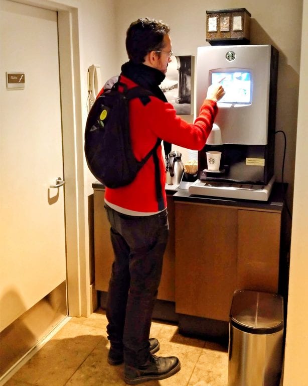 Augusto pegando um café na máquina de café da Starbucks do corredor do hotel