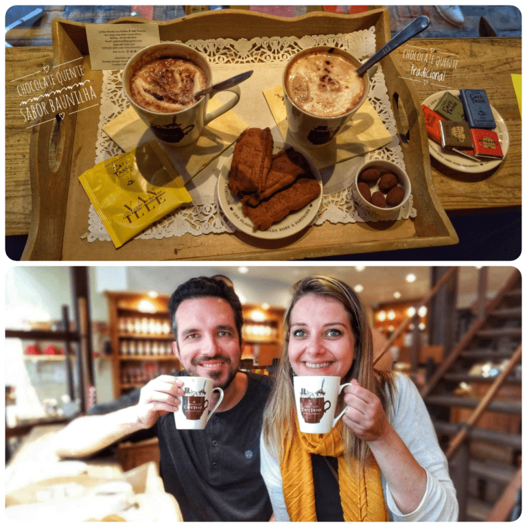 Mosaico com duas fotos. Na superior, vista de cima de uma bandeja com duas canecas de chocolate quente, barrinhas de chocolate e biscoitos em um prato. Na segunda foto, Augusto e Chai em primeiro plano sorriem segurando canecas de chocolate quente com o logo da loja com fundo desfocado.