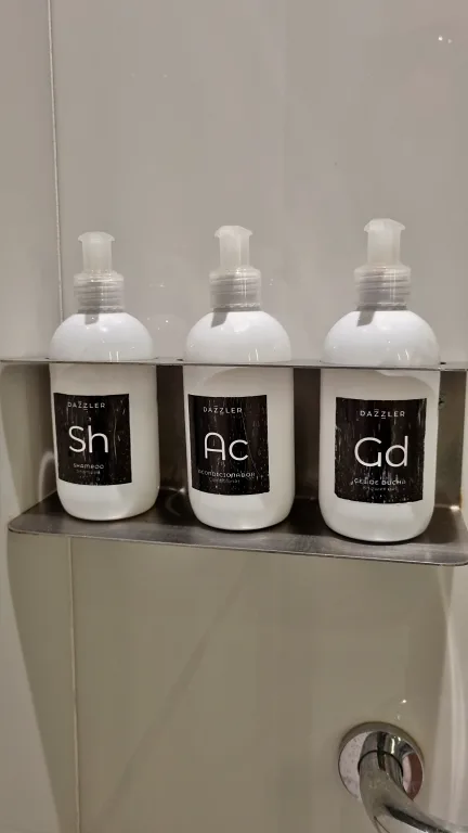 Onde ficar em La Plata: Conheça Dazzler by Wyndham La Plata 23 Três frascos de amenidades com shampoo, condicionador e gel de banho organizados em uma prateleira no chuveiro da suíte do Dazzler by Wyndham La Plata.
