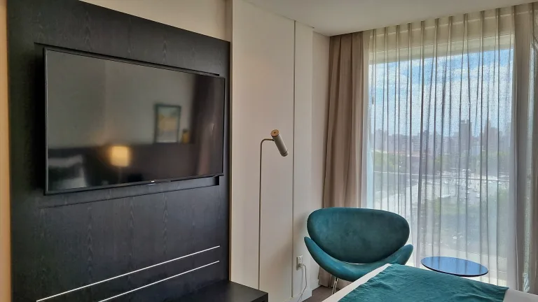 Onde ficar em La Plata: Conheça Dazzler by Wyndham La Plata 14 Quarto da suíte do Dazzler by Wyndham La Plata, com TV de tela plana, poltrona moderna e ampla janela com vista para a cidade