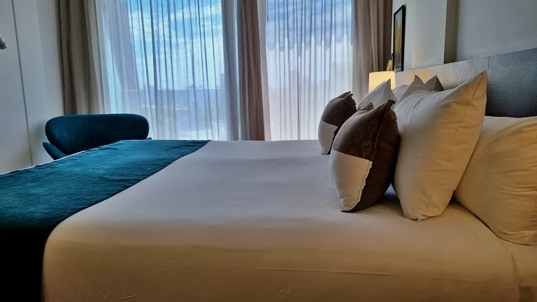 Onde ficar em La Plata: Conheça Dazzler by Wyndham La Plata 12 Cama king size no quarto da suíte do Dazzler by Wyndham La Plata, com decoração moderna, travesseiros confortáveis e uma cadeira verde ao lado da mesa