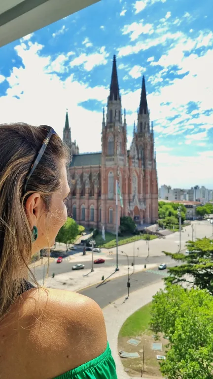 Onde ficar em La Plata: Conheça Dazzler by Wyndham La Plata 16 Chai admirando a vista da Catedral de La Plata a partir da sacada do quarto do hotel Dazzler by Wyndham La Plata, em um dia ensolarado