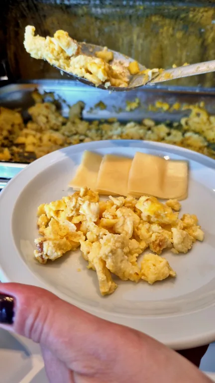 Onde ficar em La Plata: Conheça Dazzler by Wyndham La Plata 31 Prato com ovos mexidos e fatias de queijo sendo servido no buffet de café da manhã do hotel Dazzler by Wyndham La Plata."