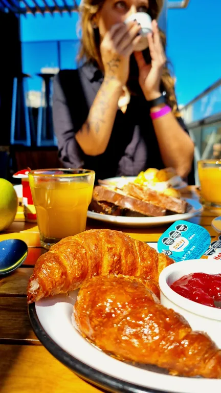 Onde ficar em La Plata: Conheça Dazzler by Wyndham La Plata 38 Café da manhã no terraço do hotel Dazzler by Wyndham La Plata, com medialunas, geleia e suco de laranja em foco, e Chai ao fundo tomando café.